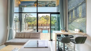 A modern room with a large window, a sofa, a table with chairs, and a view of a pool and outdoor area. - Gangneung Awesome Pension (Gangneung)