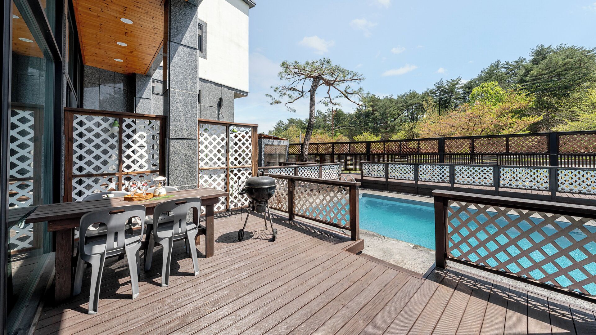 Terraza exterior con piscina, muebles de madera y una parrilla.