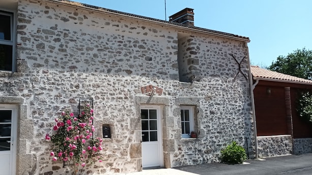 A stone building with two windows and a door, a small balcony with flowers, and a chimney. - Vendée country cottage 5 minutes from La Roche sur Yon (La Genétouze)