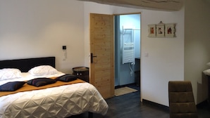 A bedroom with a bed, a wooden door, a small stool, and a wall-mounted heater. - Vendée country cottage 5 minutes from La Roche sur Yon (La Genétouze)