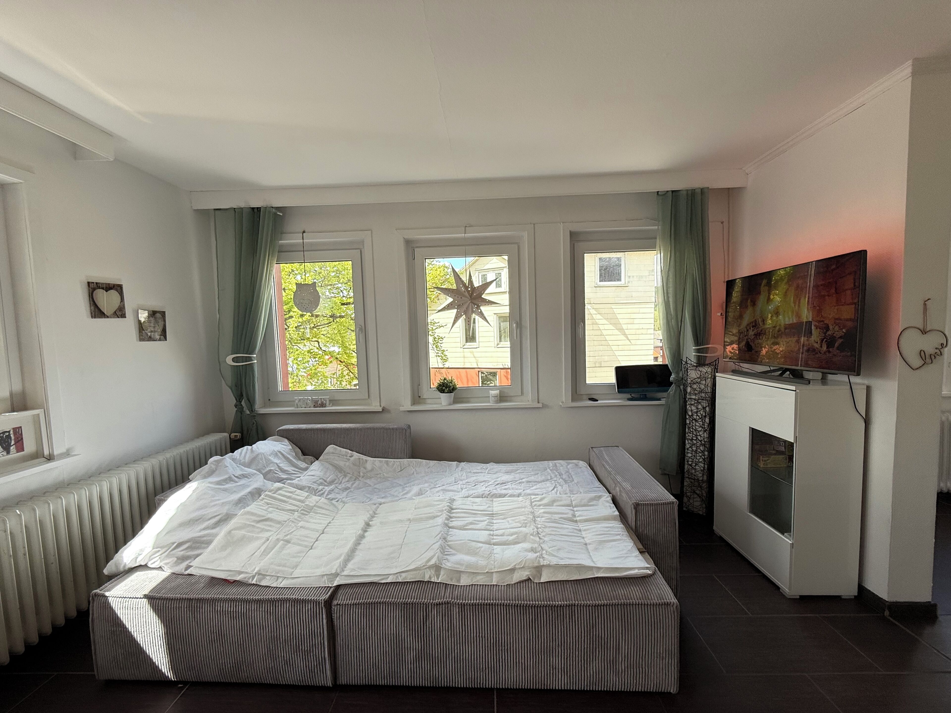 Ein Schlafzimmer mit einem großen Bett, drei Fenstern, einem Kamin und einem Fernseher.
