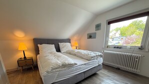 A bedroom with a bed, two bedside lamps, a radiator, and a window with a view of buildings and trees. - PrimeLoft Eule - up to 10 pers - 2 floors - balcony - modern & stylish - central (Braunlage)