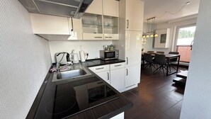 A modern kitchen with white cabinets, a black countertop, and a dining area with a table and chairs. - PrimeLoft Eule - up to 10 pers - 2 floors - balcony - modern & stylish - central (Braunlage)