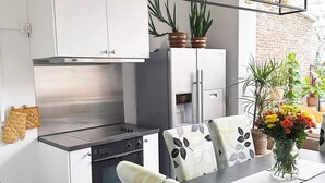 Una cocina moderna con armarios blancos, una campana extractora de acero inoxidable y una encimera negra. Hay dos plantas en macetas sobre la encimera y un jarrón con flores sobre la mesa de comedor.