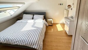 Un dormitorio con cama, mesita de noche, ventana y baño con lavabo y espejo.