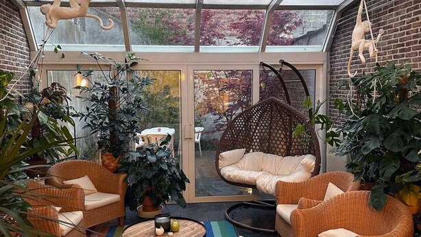 Un patio soleado con muebles de mimbre, un tapete colorido y esculturas de monos colgantes.