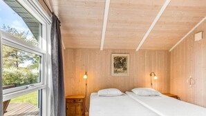 Une pièce avec deux lits, des murs en bois, une fenêtre avec des rideaux, une petite armoire en bois et un tableau accroché au mur.