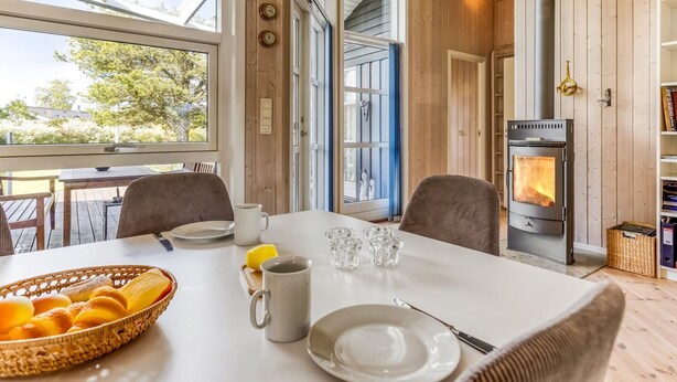 Une pièce chaleureuse avec un décor intérieur en bois, une grande fenêtre, une table mise pour le petit-déjeuner et un poêle à bois.