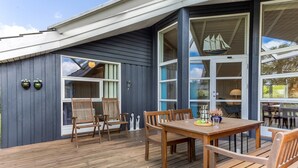Une terrasse en bois avec une table et des chaises, une grande fenêtre et une décoration sur le thème d’un voilier.