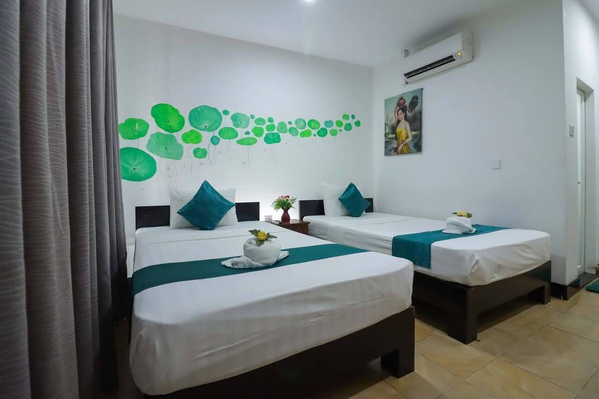 A hotel room with two beds, each with a white bedspread and teal accents, a wall mural of green circles, and a painting above the bed.