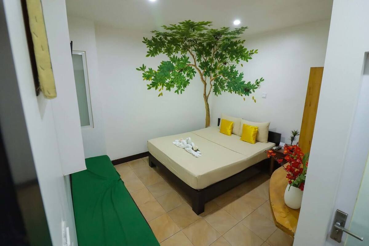A bedroom with a bed, a green sofa, a potted plant, and a wall-mounted artificial tree.