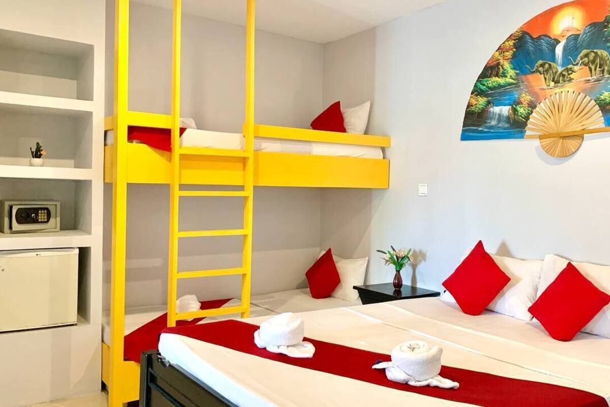 A room with a bunk bed, a small desk with a radio, a painting of elephants, and towels on the bed.