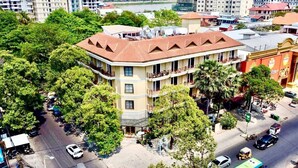 Ein mehrstöckiges Hotel mit rotem Ziegeldach, umgeben von üppiger Vegetation und einer belebten Straße.