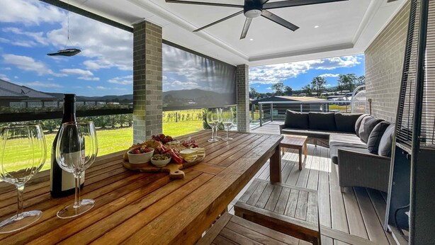 Un patio amplio con mesa de madera listo para comer, un ventilador de techo y vistas a un viñedo.