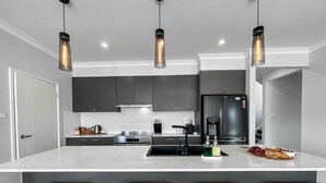 Una cocina moderna con una isla grande, taburetes de bar, electrodomésticos de acero inoxidable e iluminación colgante.
