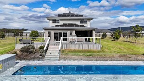 Una casa moderna de dos pisos con una terraza amplia, una piscina y vistas del paisaje circundante.