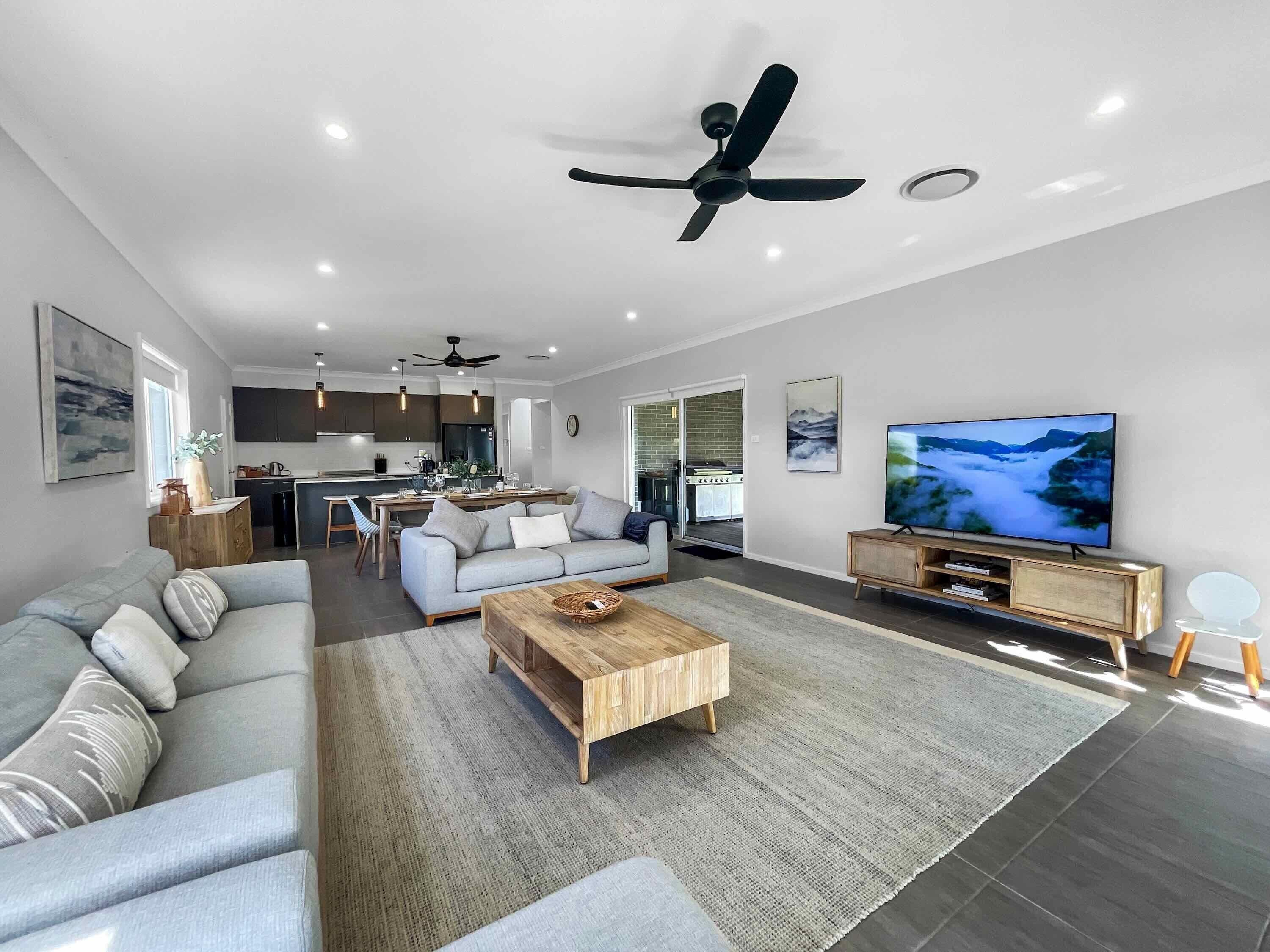 Una sala de estar moderna con un sofá gris, una mesa de centro de madera y un televisor sobre un mueble de madera.