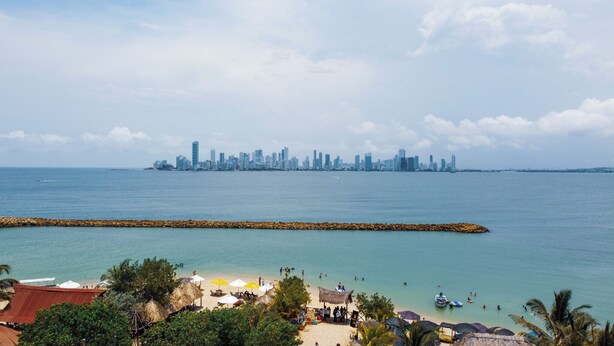 A beach with a city skyline in the background, a breakwater, and beach umbrellas. - Perla Negra House Hostel (Cartagena)