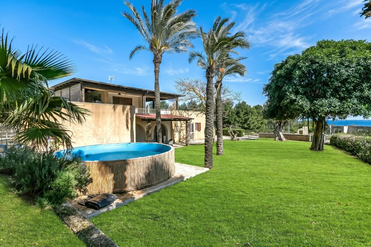 A modern house with a swimming pool, palm trees, and a well-maintained lawn.