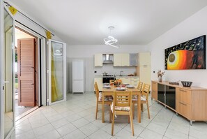 A modern kitchen with a dining area, featuring a large painting, a unique light fixture, and a sliding glass door leading to an outdoor area. - Riva Blu Apartments (Santa Cesarea Terme)