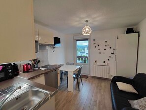 Una cocina compacta con comedor, un sofá negro y una ventana con vistas a una casa.
