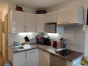Una cucina compatta con mobili bianchi, forno integrato, microonde e lavello.