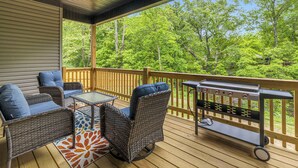 A covered outdoor deck with wicker furniture, a grill, and a view of a forest. - Discoverer - Ozark Mountain Retreat - Pets Allowed (Bella Vista)