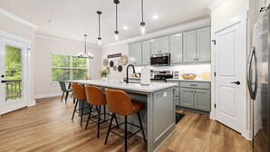 A modern kitchen with a central island, bar stools, a microwave, and a refrigerator. - Discoverer - Ozark Mountain Retreat - Pets Allowed (Bella Vista)