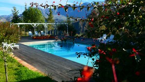 A swimming pool with a wooden deck, surrounded by greenery and white lounge chairs. - Le Case di Cardellino - AgriSpa (Sclafani Bagni)