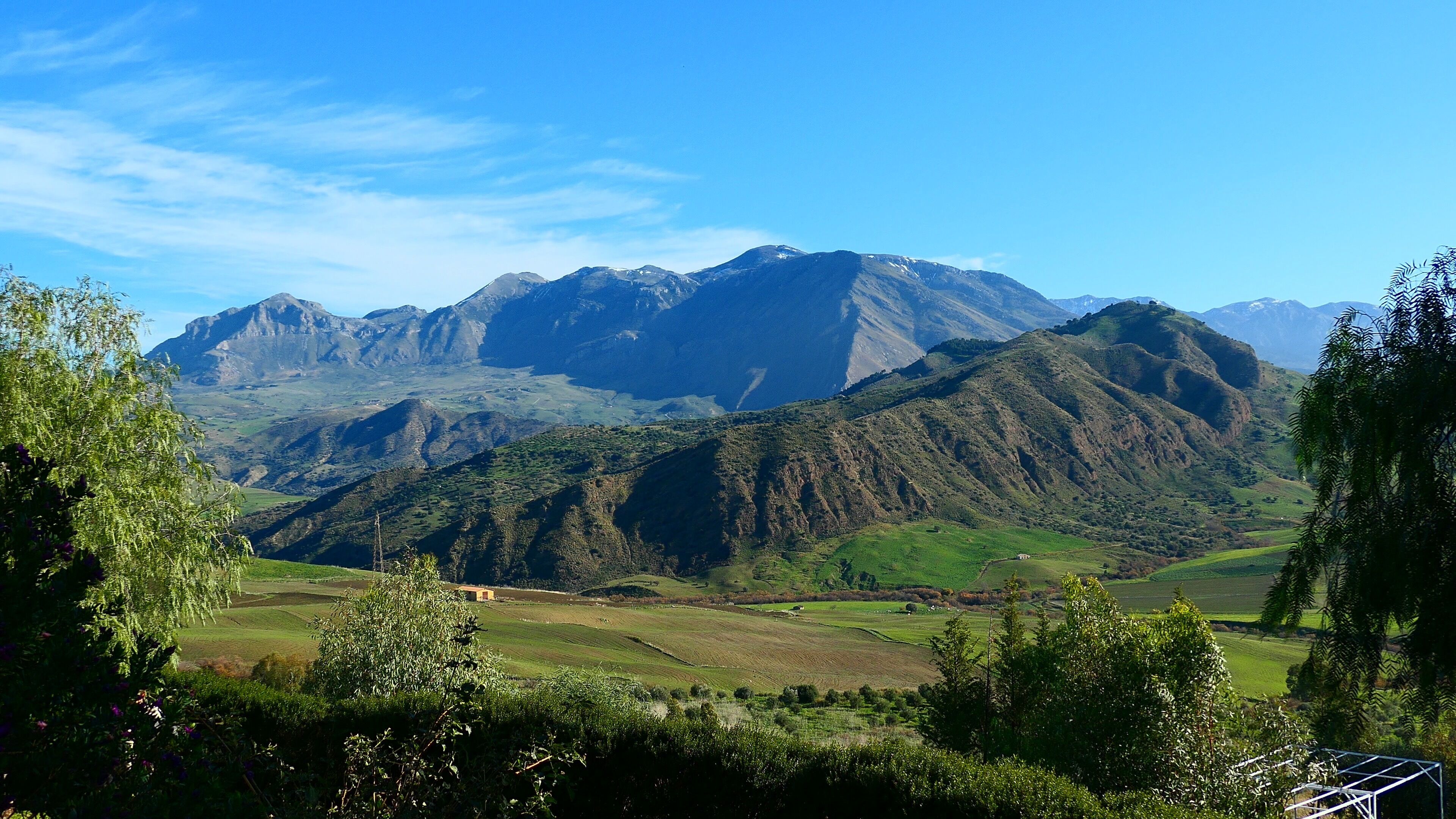 Eine gebirgige Landschaft mit grünen Feldern und blauem Himmel.
