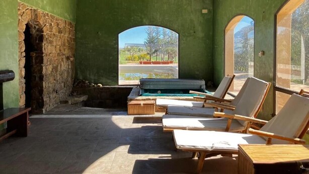 A sunlit room with a stone wall, a stone fireplace, and a pool area with lounge chairs. - Le Case di Cardellino - AgriSpa (Sclafani Bagni)