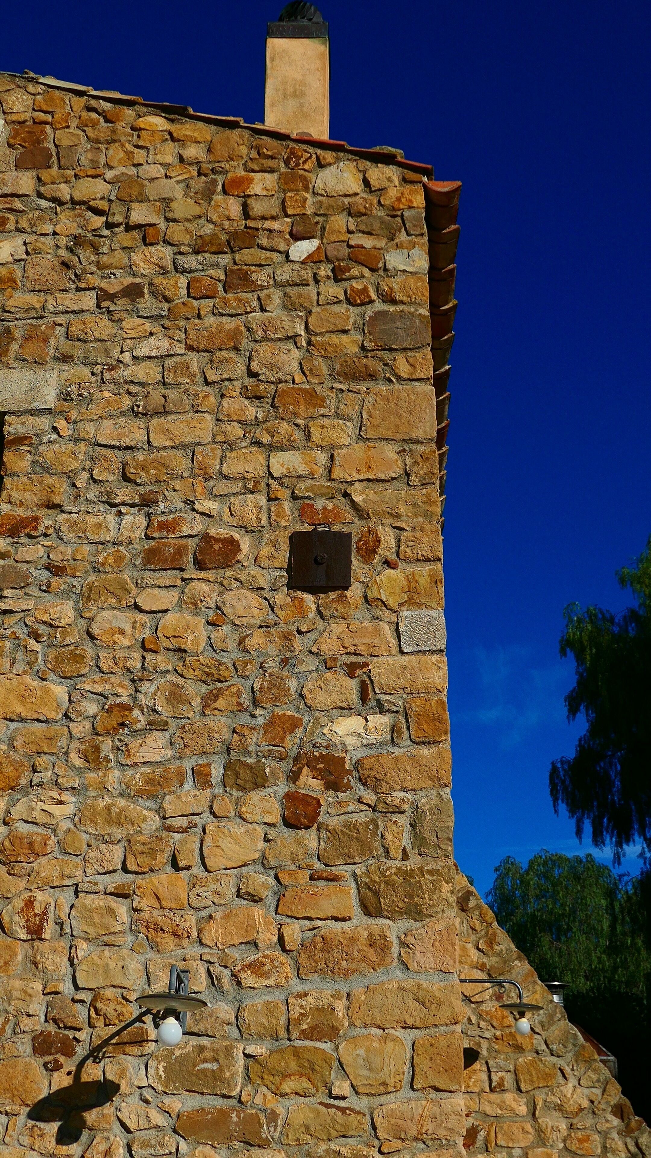 Ein Steinhaus mit Schornstein, einem kleinen quadratischen Fenster und einer Straßenlaterne.