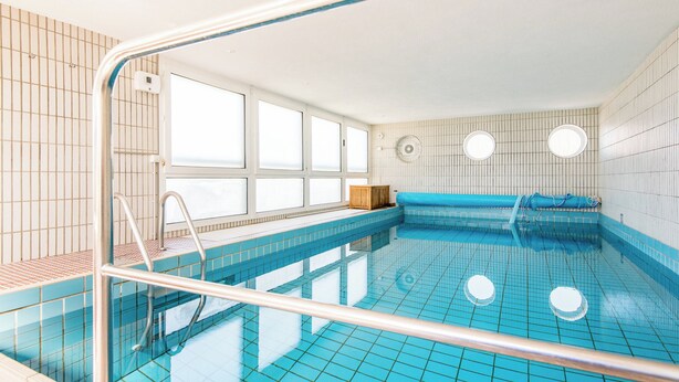 Una piscina con baldosas azules cristalinas, un banco de madera y una escalera metálica.