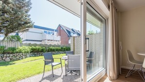 Una habitación moderna con un ventanal corredero que da a un patio con mobiliario exterior y vistas a una casa de ladrillo y jardín.