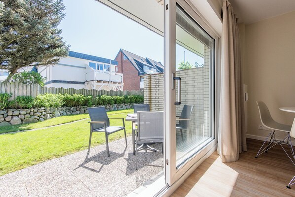 Ein modernes Zimmer mit einer Schiebetür zu einer Terrasse mit Sitzgelegenheit und Blick auf ein Backsteinhaus und einen Garten.