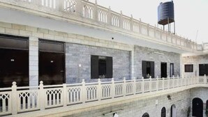 A two-story building with a balcony, a water tank on the roof, and a courtyard with a fountain.