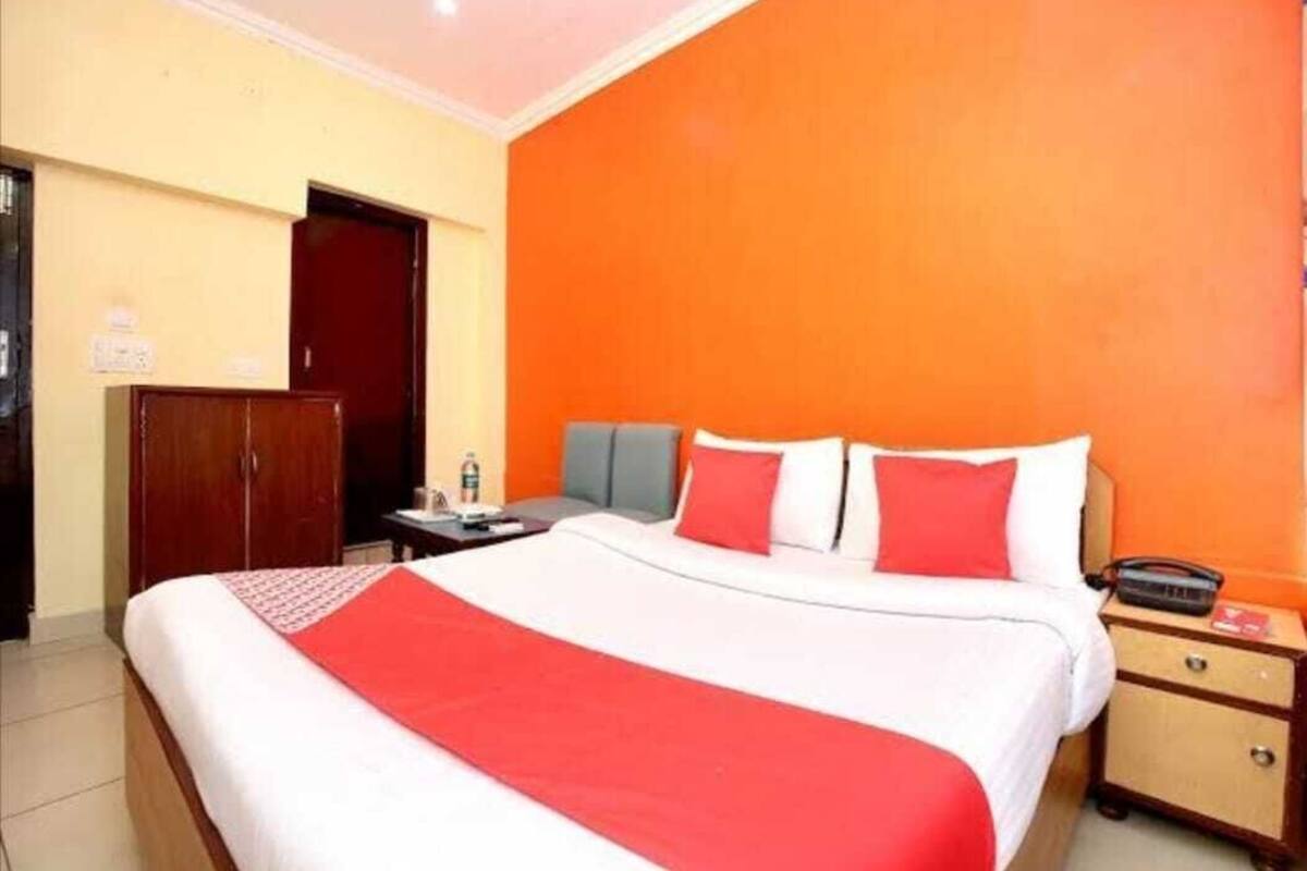 Une chambre d’hôtel avec un grand lit, une table de chevet, une armoire et un mur de couleur orange.