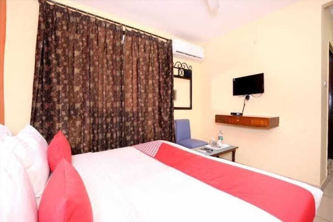 A hotel room with a bed, a chair, a small table, a TV, and a curtain.
