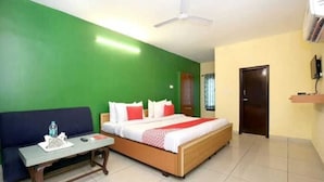 A hotel room with a bed, a sofa, a small table, and a ceiling fan.