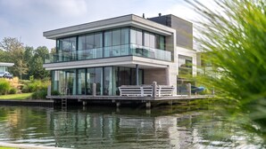 A modern two-story house with large glass windows, a wooden deck, and a view of a body of water. - Dormio Harbour Village (Arnemuiden)