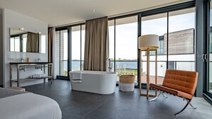 A modern hotel room with a large bathtub, a sitting area with a view, and a balcony with a view of the water. - Dormio Harbour Village (Arnemuiden)