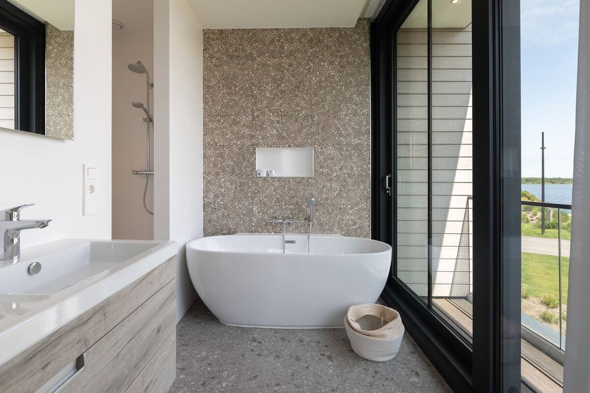 Une salle de bain moderne avec une baignoire sur pieds, un grand miroir et une vue sur l’extérieur.