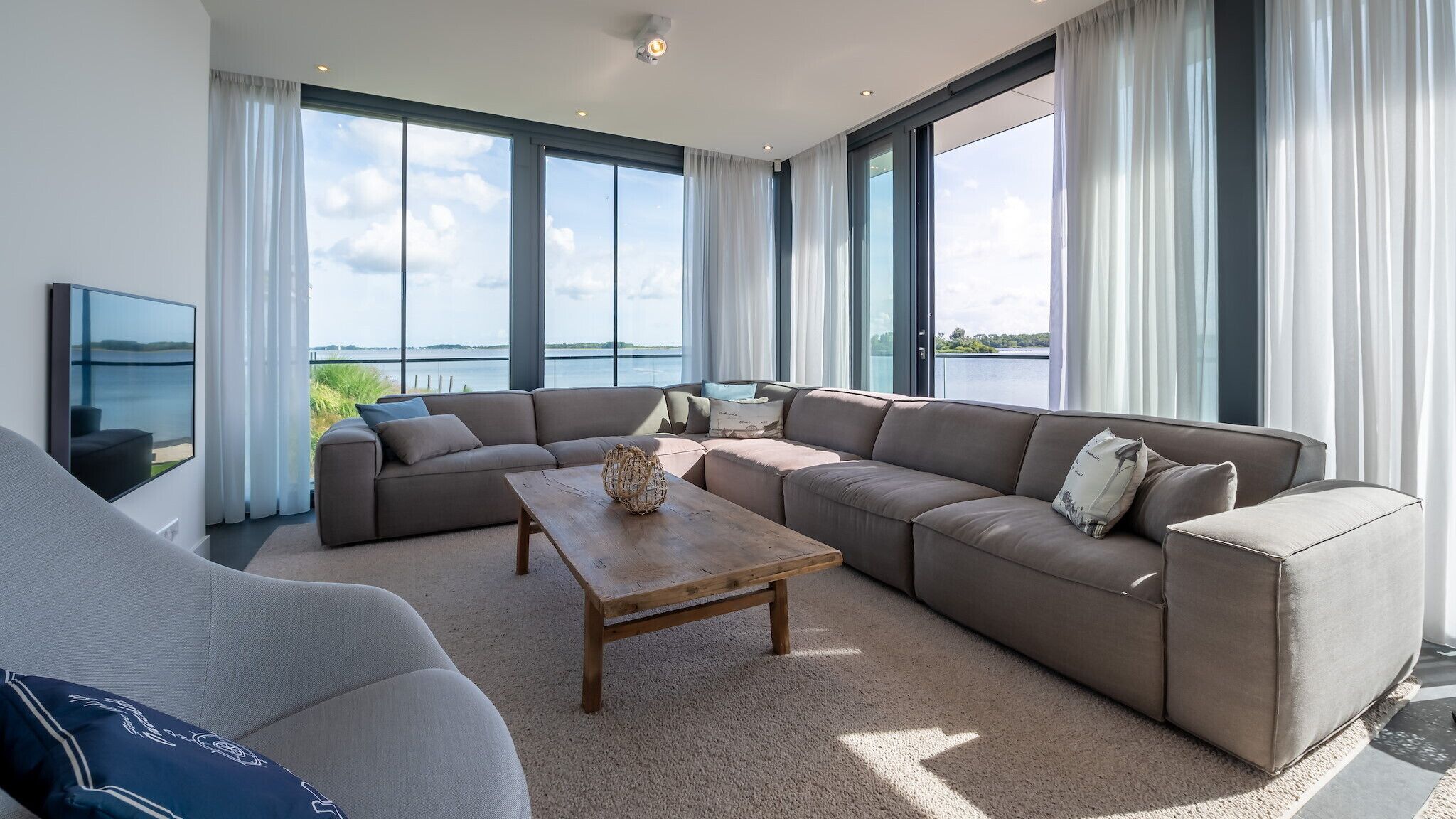 A modern living room with a large sectional sofa, a coffee table, and a TV on the wall.