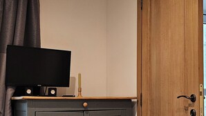 A bedroom with a bed, a television on a dresser, a wooden door, and a window with curtains. - Like at Home: Apartment near the forest with office and terrace (Liège)
