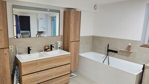 A modern bathroom with a wooden vanity, two sinks, a large mirror, and a bathtub. - Like at Home: Apartment near the forest with office and terrace (Liège)