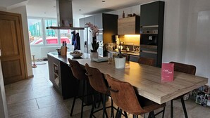 A modern kitchen with a wooden dining table, bar stools, and a kitchen island. - Like at Home: Apartment near the forest with office and terrace (Liège)