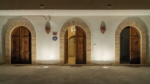 Eine Gebäudefassade mit drei Rundbogenportalen, jedes mit einer Holztür und einem kleinen, dekorativen Wappen darüber.