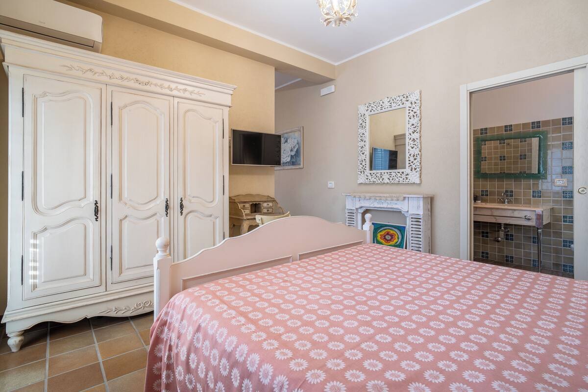 A bedroom with a bed, a wardrobe, a mirror, and a bathroom visible through an open door.