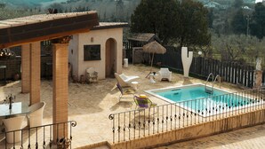 Ein Poolbereich mit einer Pergola, Liegestühlen und einem kleinen Gebäude.