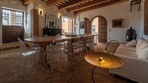 Ein geräumiger Essbereich mit Holztisch und transparenten Stühlen, Steinboden und einem weißen Sofa mit Lampe.